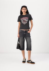 Black graphic t-shirt with red "CHERRY" print and floral design, paired with gray denim culottes and black sneakers with beige laces.
