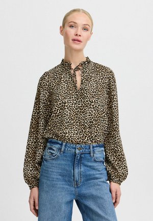 Leopardmönstrad blus i beige och brunt siden, med knytkrage, långa puffärmar och en avslappnad passform, ihop med högmidjade blå jeans.