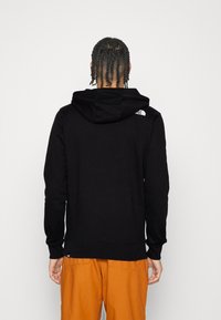 Felpa nera con cappuccio realizzata in tessuto morbido, dotata di tasca a marsupio, cappuccio regolabile con cordino e una accentuazione del logo bianco sulla spalla.