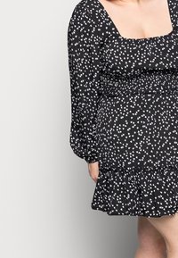 Svart klänning med vita hjärtmönster, fyrkantig halsringning, långa puffärmar och en volangnederdel. Tillverkad av lätt tyg.