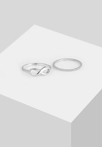 Două inele argintii pe o suprafață deschisă: unul are un simbol de infinit, iar celălalt are un design de frânghie răsucită. Ambele sunt lustruite cu un finisaj strălucitor.