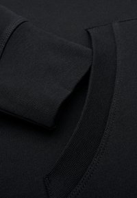 Prenda negra de manga larga con puños y cuello acanalados, con detalles de costura visibles en la tela suave.