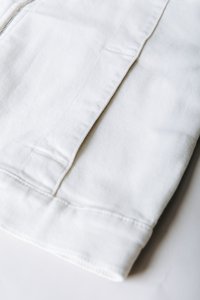 Λευκό βαμβακερό ύφασμα με υφή, με ραμμένες ραφές και επίπεδο τελείωμα. Το υλικό φαίνεται ανθεκτικό και ελαφρύ.