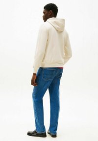 Felpa con cappuccio color crema con coulisse, abbinata a jeans blu e scarpe nere. La felpa ha una texture liscia e una vestibilità comoda.