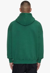 Grøn bomulds-hoodie med en rummelig pasform, hætte og elastiske manchetter. Har en glat tekstur og ribbet kant, vist fra bagsiden.