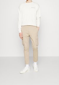 Beige cargo kalhoty s bočními kapsami, zúžený střih. V kombinaci se světložlutým dlouhým rukávem a bílými teniskami. Jednoduchý, funkční design.