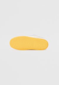 Sapatilha branca com uma sola de borracha texturizada; com um fundo amarelo e uma superfície superior lisa, projetada com acentos mínimos.