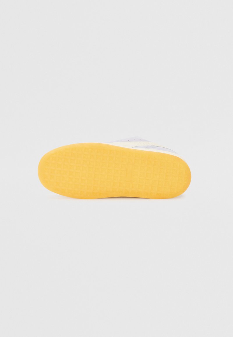 Baskets blanches avec une semelle en caoutchouc texturée ; présentant un fond jaune et une surface supérieure lisse, conçues avec des accents minimaux.