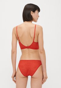 Piros fehérnemű szett sima, mintás anyagból; állítható pántok a melltartón és varrás nélküli kialakítás a bugyin.