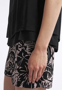 Haut superposé noir porté sur un short présentant un motif floral en noir et rose clair. Le short a une texture lisse et une coupe décontractée.