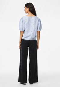 Light blue blouse with short puff sleeves, featuring a check pattern and small red floral embroidery. Paired with black wide-leg pants.