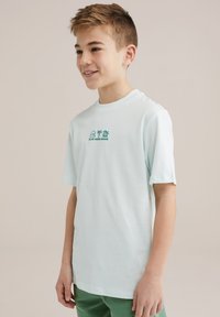 T-maica svetlo mint zelene barve iz mehkega in gladkega materiala. Ima okroglo ovratnico in kratke rokave, na sprednji strani pa je natisnjen napis "BLUE RIDGE DENIM" ter grafični elementi.