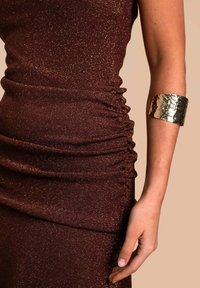 Burgunderfarbendes Glitzerkleid mit gerafftem Stoff, ergänzt durch ein texturiertes goldenes Metallarmband. Glatte Textur mit metallischen Akzenten.
