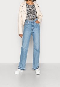 Krämfärgad läderbikerjacka, blommönstrad svart topp, ljusblå högmidjade raka jeans och vita plattformssneakers.