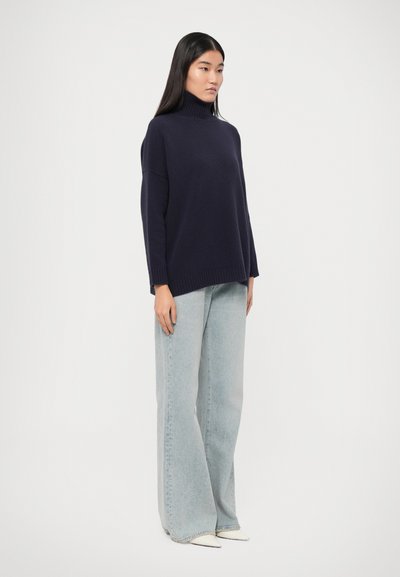 Navy turtleneck sweater with a relaxed fit, paired with light blue wide-leg jeans and pointed white shoes. Simple, smooth texture.