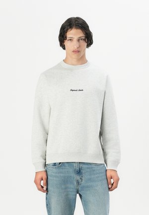 Gray cotton crewneck sweatshirt with ribbed cuffs and hem; features "Original Studio" logo in black on the chest; paired with light blue jeans.
