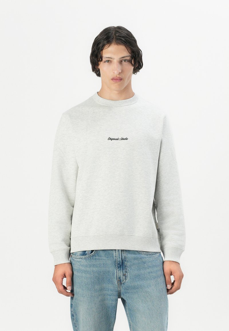 Grijze katoenen sweatshirt met ronde hals en ribgebreide boorden en zoom; met het 'Original Studio' logo in het zwart op de borst; gecombineerd met lichtblauwe jeans.