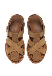 Brown suede sandals featuring cross straps, a rounded toe, and a textured sole. The design includes a side zip for easy wear.