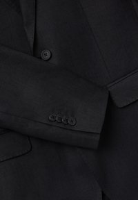 Chaqueta de traje negra con una textura suave, cierre de un solo botón y cuatro botones negros en los puños. Detalle del solapa en ángulo y del bolsillo visible.