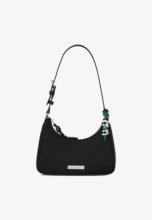 Crna torba na rame s podesivim remenom, srebrna oznaka brenda i mali zeleni i bijeli čarobni likovi privjesci na strani.