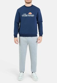 Granatowy nieformalny sweter z logo "ellesse", w zestawieniu z jasnoszarymi spodniami dresowymi. Białe trampki z teksturowaną podeszwą. Prosty i casualowy design.