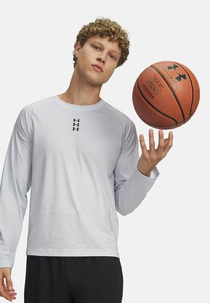 Langärmliges weißes Sportshirt mit feiner horizontaler Struktur und schwarzem Logo, gehalten von einer Person, die einen Basketball balanciert.