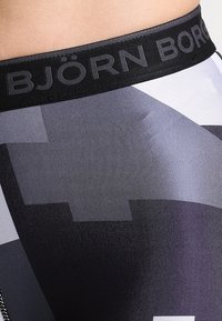 Fascia elastica nera con logo "BJÖRN BORG", caratterizzata da un tessuto a motivi nelle tonalità di grigio, con una texture liscia e opaca.