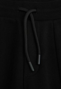 Czarne bawełniane spodnie dresowe z żebrowanym pasem i sznurkiem, charakteryzujące się teksturowanym materiałem oraz metalowymi końcówkami sznurka.