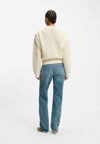 Chunky cream sweater with ribbed texture, rounded shoulders, and fitted cuffs, paired with light blue wide-leg jeans and pointed beige shoes.