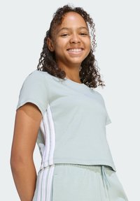 Svetlozelené tričko s krátkym rukávom a skráteným strihom, s bielymi pruhovanými akcentmi na bokoch a malým logom na hrudi.