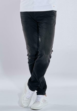Dunkelblaue Jeans im Straight-Leg-Schnitt mit subtiler Struktur, kombiniert mit weißen Sneakers mit Schnürdesign und kontrastierenden Akzenten.