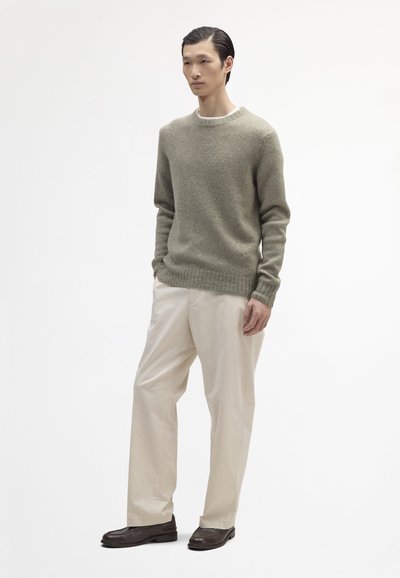 Maglione di lana verde chiaro con scollatura tonda, abbinato a pantaloni crema a sigaretta e mocassini marrone scuro, in piedi su uno sfondo bianco.