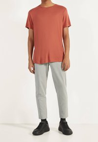 Rostfärgad kortärmad t-shirt kombinerad med ljusgrå tapered byxor och svarta sneakers, vilket visar en avslappnad och lätt design.