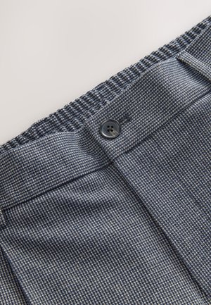 Tissu texturé bleu foncé avec un motif subtil. Doté d'une fermeture par bouton et d'une ceinture élastique, offrant flexibilité et confort.