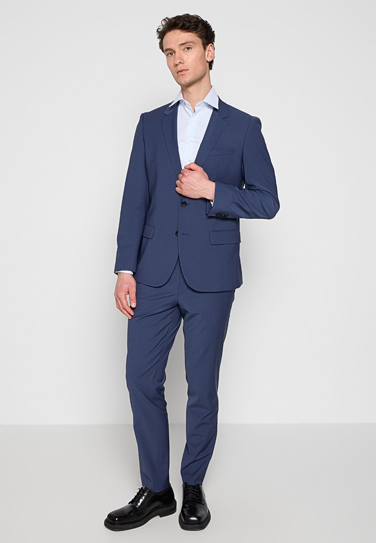 Abito blu navy con giacca a un petto e pantaloni coordinati. Tessuto liscio con una sottile trama. Scarpe eleganti nere completano l'outfit.