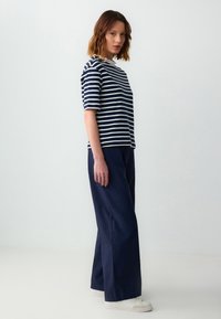 Chemise à rayures bleu marine et blanche à manches courtes associée à un pantalon large bleu marine. Le tissu semble lisse, avec un détail de col contrastant.