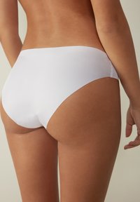 Weißer Bikiniunterteil aus glattem, dehnbarem Material mit einem tiefen Schnitt und minimaler Abdeckung auf der Rückseite, akzentuiert durch ein nahtloses Design.