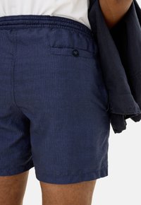 Pantaloni corti blu navy, texturizzati, con vita elastica e una tasca posteriore con bottone. Lunghezza corta, design casual.