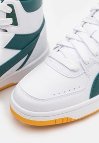 Wysokie sneakersy z białą skórzaną powierzchnią, akcentami w kolorze teal, teksturowanymi nakładkami oraz żółtą gumową podeszwą. Sznurówki są białe.