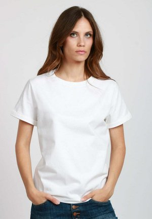 Maglietta bianca a maniche corte con scollatura rotonda, realizzata in cotone. Presenta maniche arrotolate e una vestibilità morbida. Abbinata a jeans blu.