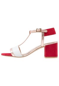 Sandales pour femmes avec une bride métallique en or rose, un bandeau avant blanc et un talon bloc en daim rouge. Design à bride T avec fermeture à boucle à la cheville.