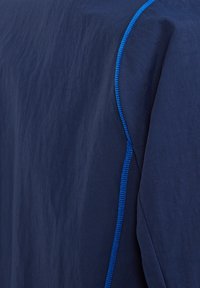 Marineblaues Kleidungsstück mit einer strukturierten Oberfläche, das einen kontrastierenden hellblauen Saum entlang der Kante aufweist. Einfaches, elegantes Design, keine Muster.