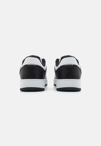 Sort og hvide sneakers med en glat læderoverdel, polstret krave og struktureret gummisål, der har minimal branding på hælen.