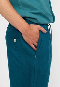 Cyaan broek van textuurstof, met een zijzak met een rits en een zichtbaar label. Touwtjes in de taille voor een verstelbare pasvorm.