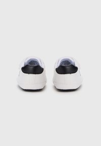 Λευκά αθλητικά παπούτσια με λείο φινίρισμα, με μαύρο δερμάτινο τμήμα στη φτέρνα και υφασμάτινη εσωτερική επένδυση με υφή. Κλασικός σχεδιασμός με κορδόνια και λαστιχένια σόλα.