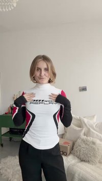 Wit, nauwsluitend sportshirt met lange mouwen en rode en zwarte accentpanelen. Voorzien van een logo op de borst en duimgaten in de manchetten.