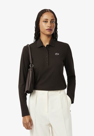 Polo shirt lungo a maniche con pulsante in tre pezzi di colore marrone scuro, con un piccolo logo ricamato. Abbinato a pantaloni bianchi su misura e una borsa scura.