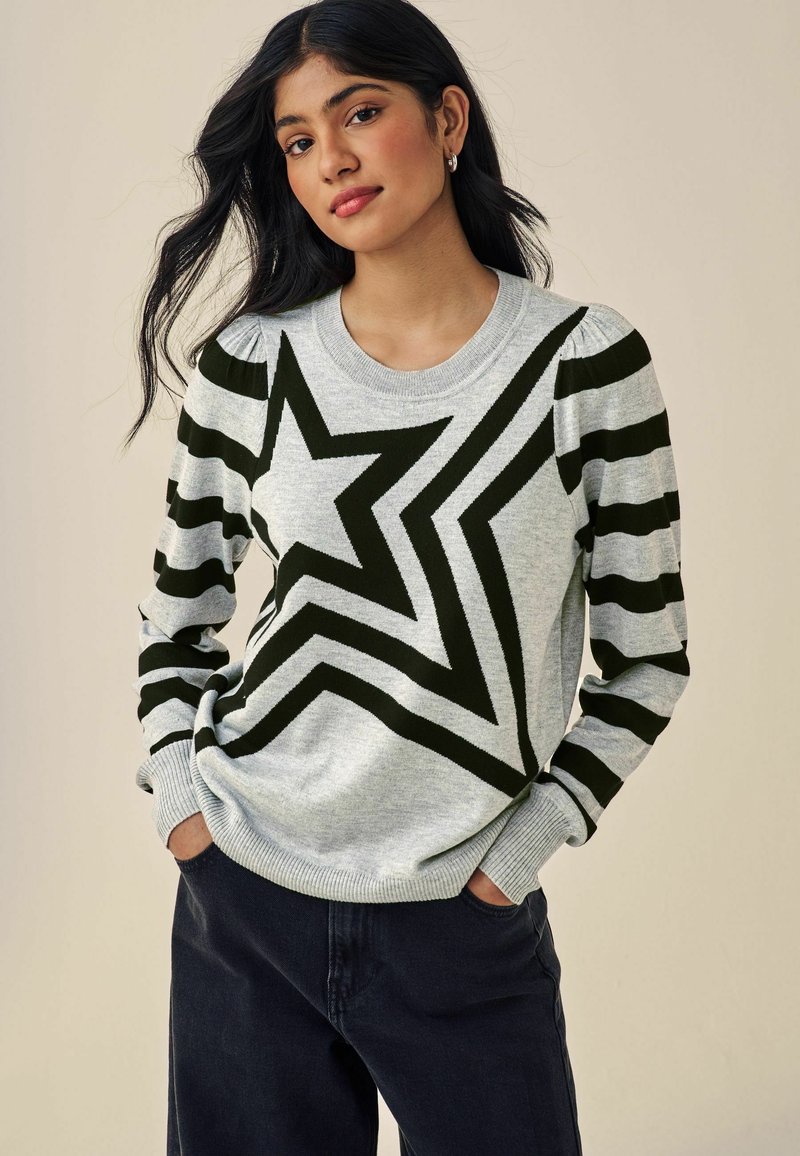 Pull en tricot gris avec un grand motif d'étoile noire et des manches rayées noires. Les poignets et l'ourlet côtelés complètent la coupe décontractée.