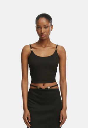 Donna che indossa un top corto nero a coste con spalline sottili e una gonna abbinata a vita alta con accenti dorati decorativi su spalline e vita.