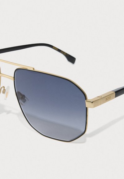 Lunettes de soleil avec monture dorée, verres hexagonaux dégradés bleus et embouts de branches noirs, gravées "BOSS" sur la charnière de la branche.
